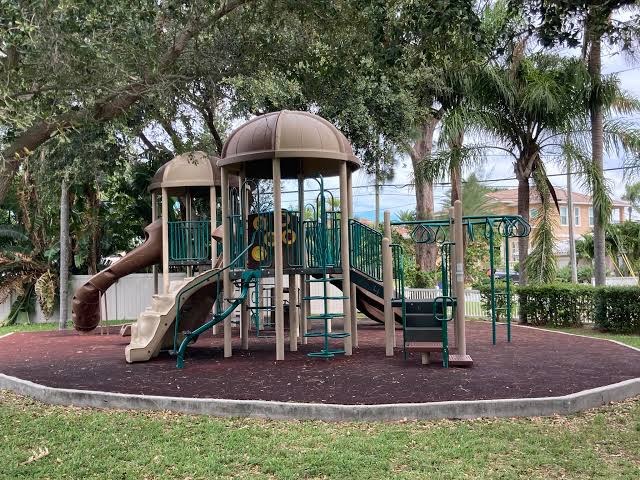 Shaded children's playground with slides and climbing bars under oak trees and palms at Brown Park in Indian Rocks Beach