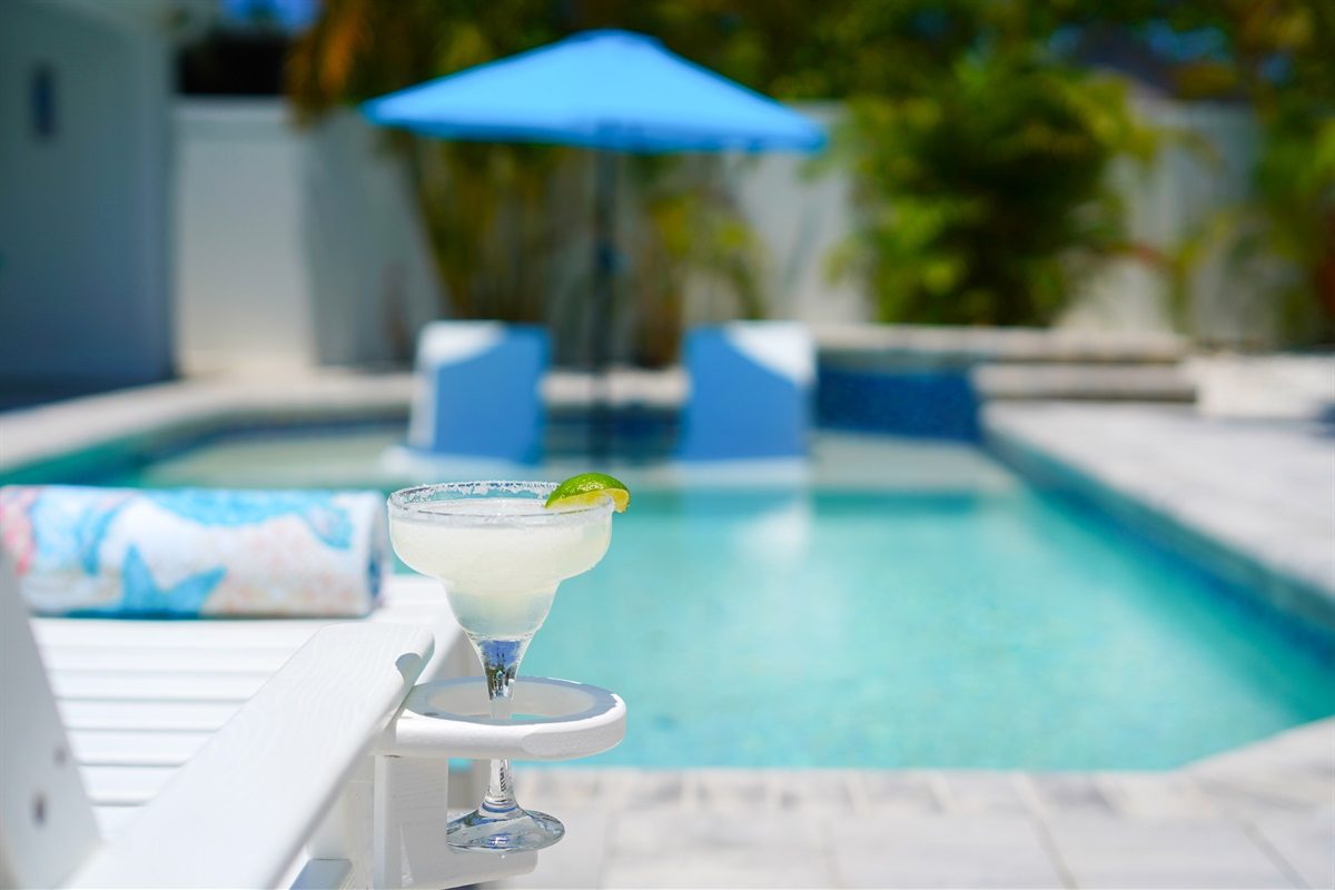 Coastal Charm heated pool with a sun shelf, loungers and an umbrella