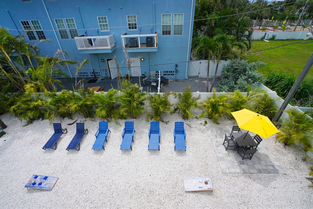 Aerial view of the sandy yard with blue loungers and cornhole at Coastal Getaway