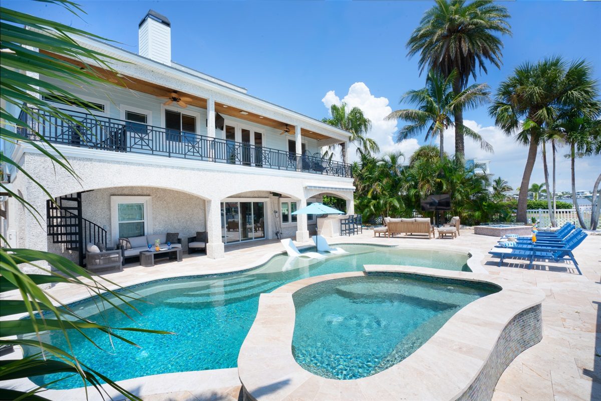 Coastal Manor heated pool and spa beside the two-story home with balconies and palm trees