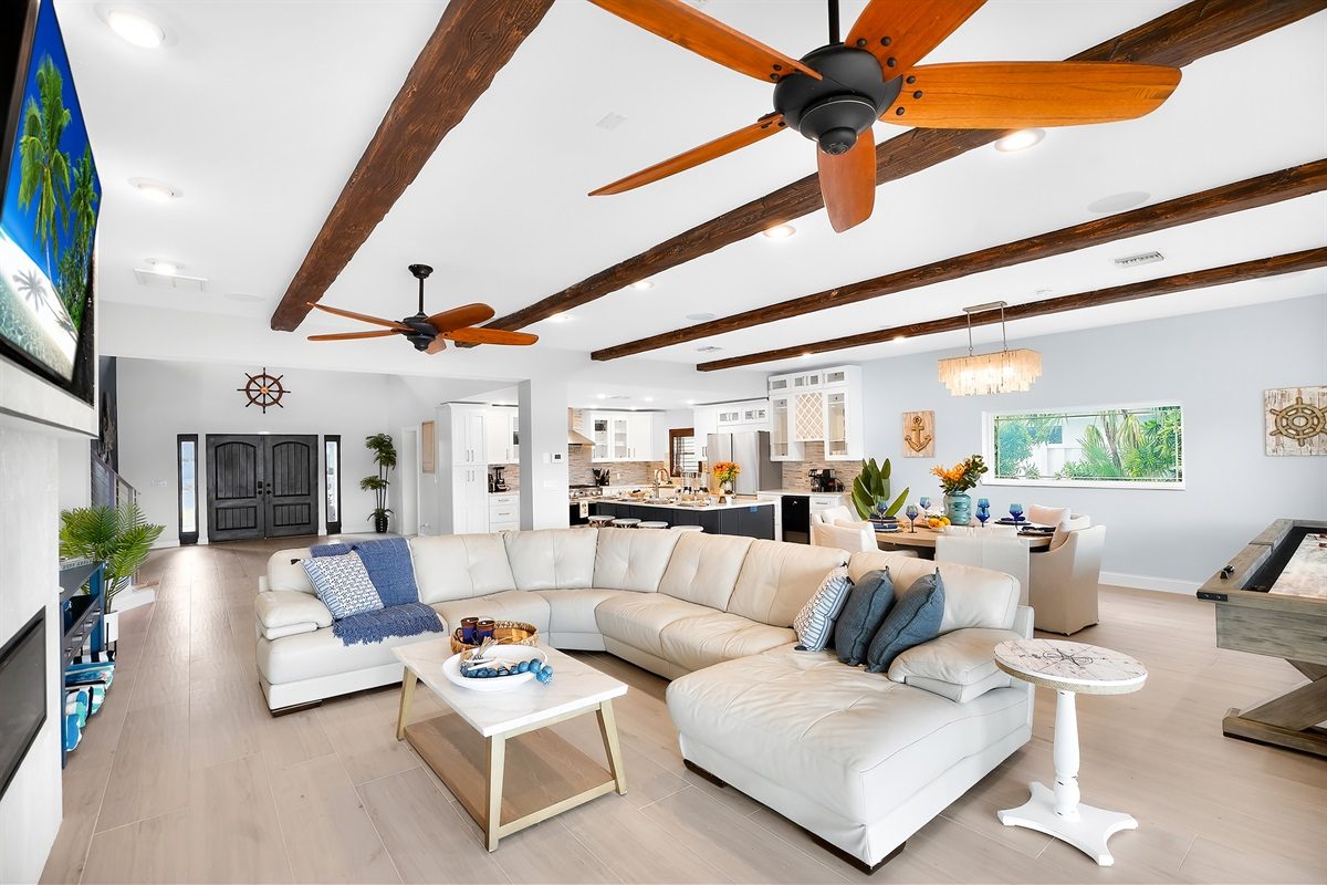 Open living room with a white sectional and wood-beamed ceiling at Coastal Manor