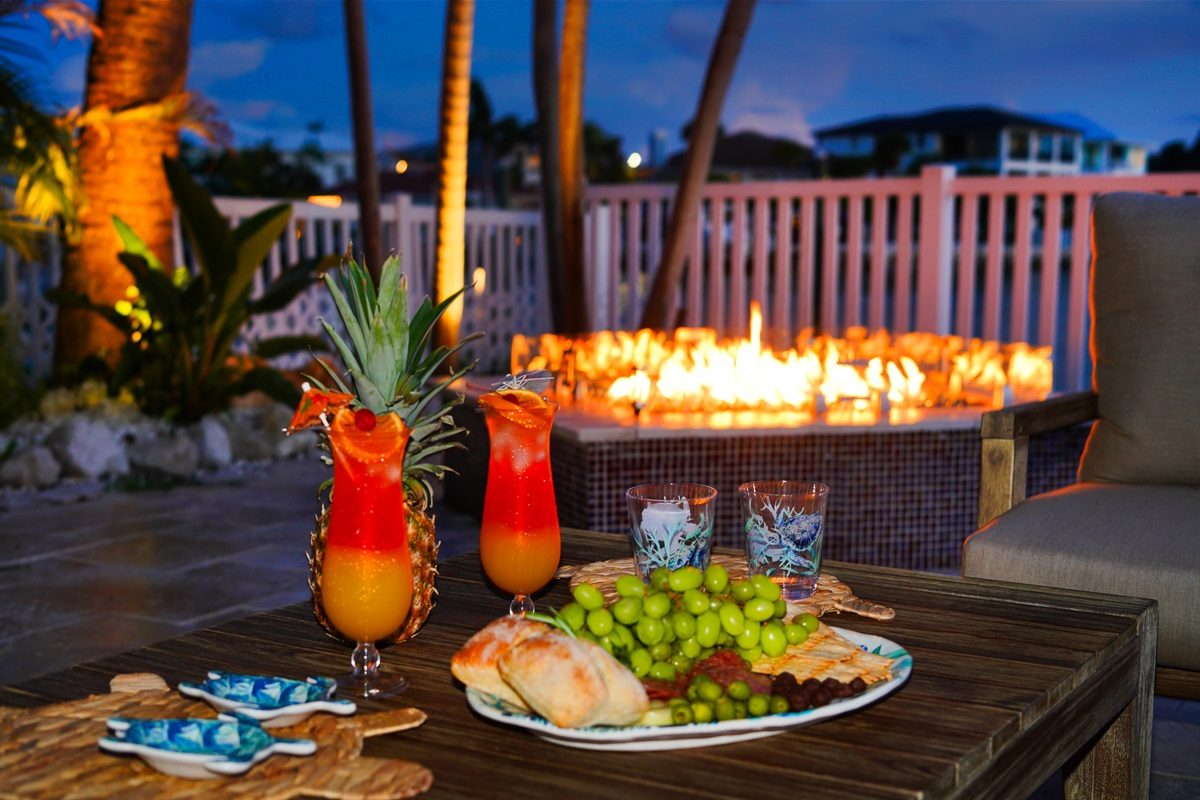 Fire pit with tropical drinks and a fruit platter at dusk at Coastal Manor