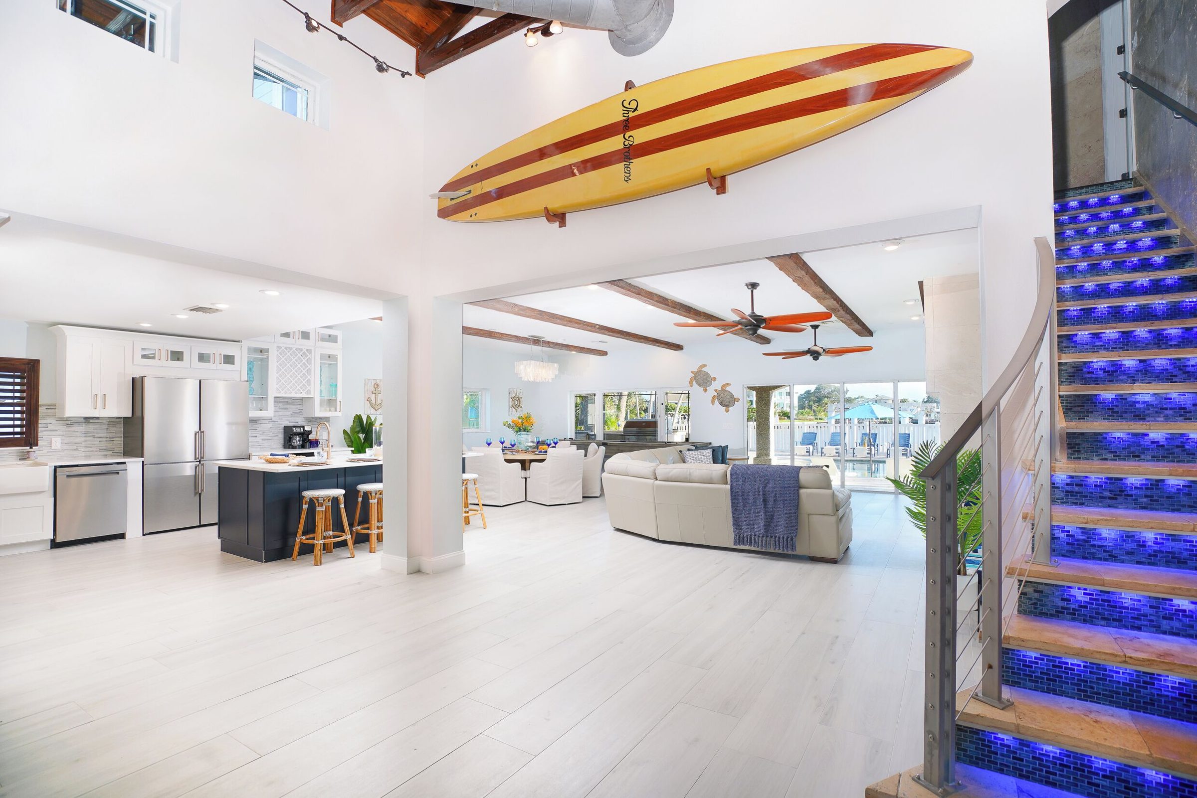 Open-plan living, dining and kitchen with a blue-lit staircase at Coastal Manor