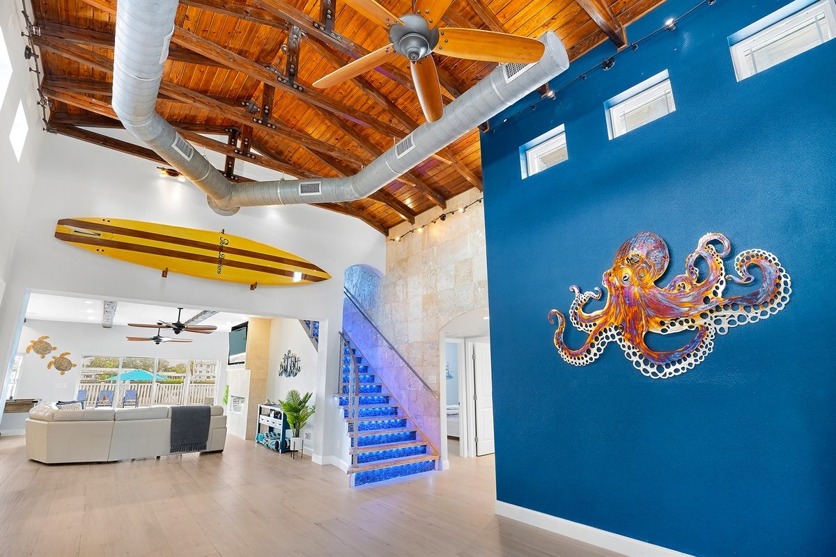 Entry hall with a surfboard, octopus mural and lit staircase at Coastal Manor