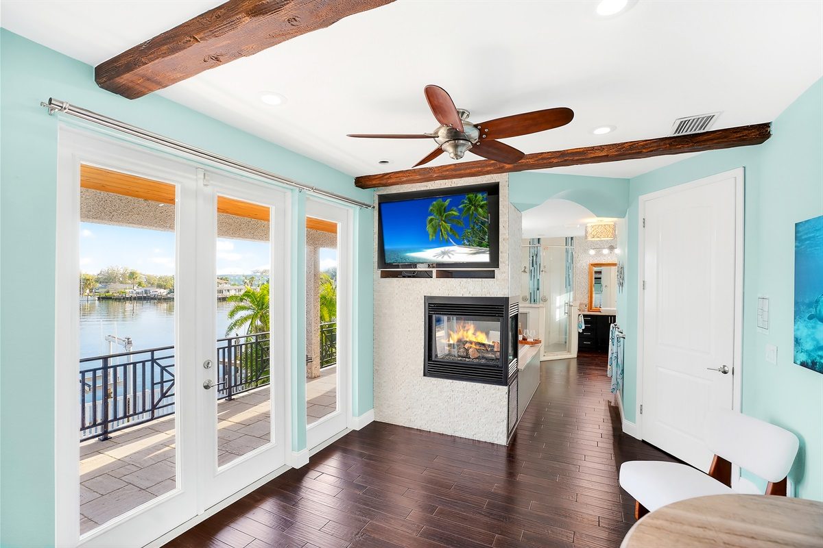 Primary suite with a fireplace, TV and French doors to a waterfront balcony at Coastal Manor