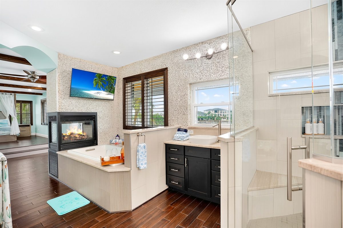 Primary bathroom with a soaking tub, fireplace and glass shower at Coastal Manor
