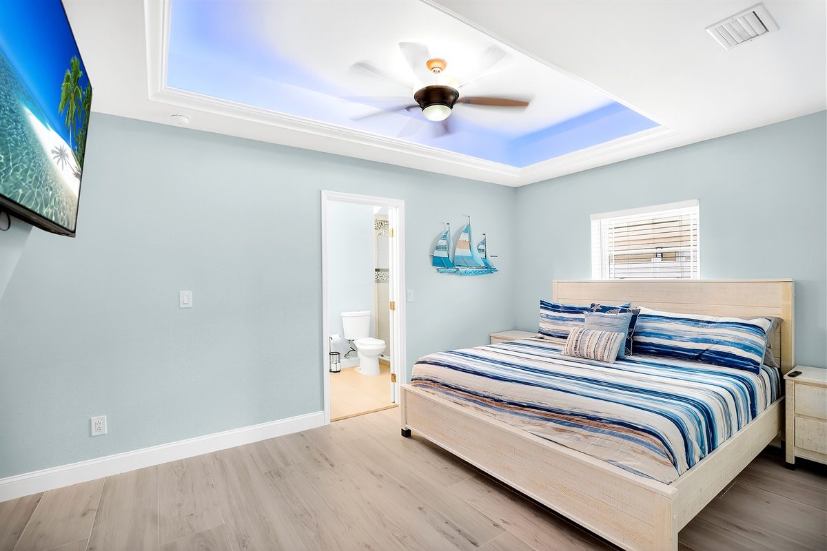 Bedroom with striped bedding and a blue-lit tray ceiling at Coastal Manor