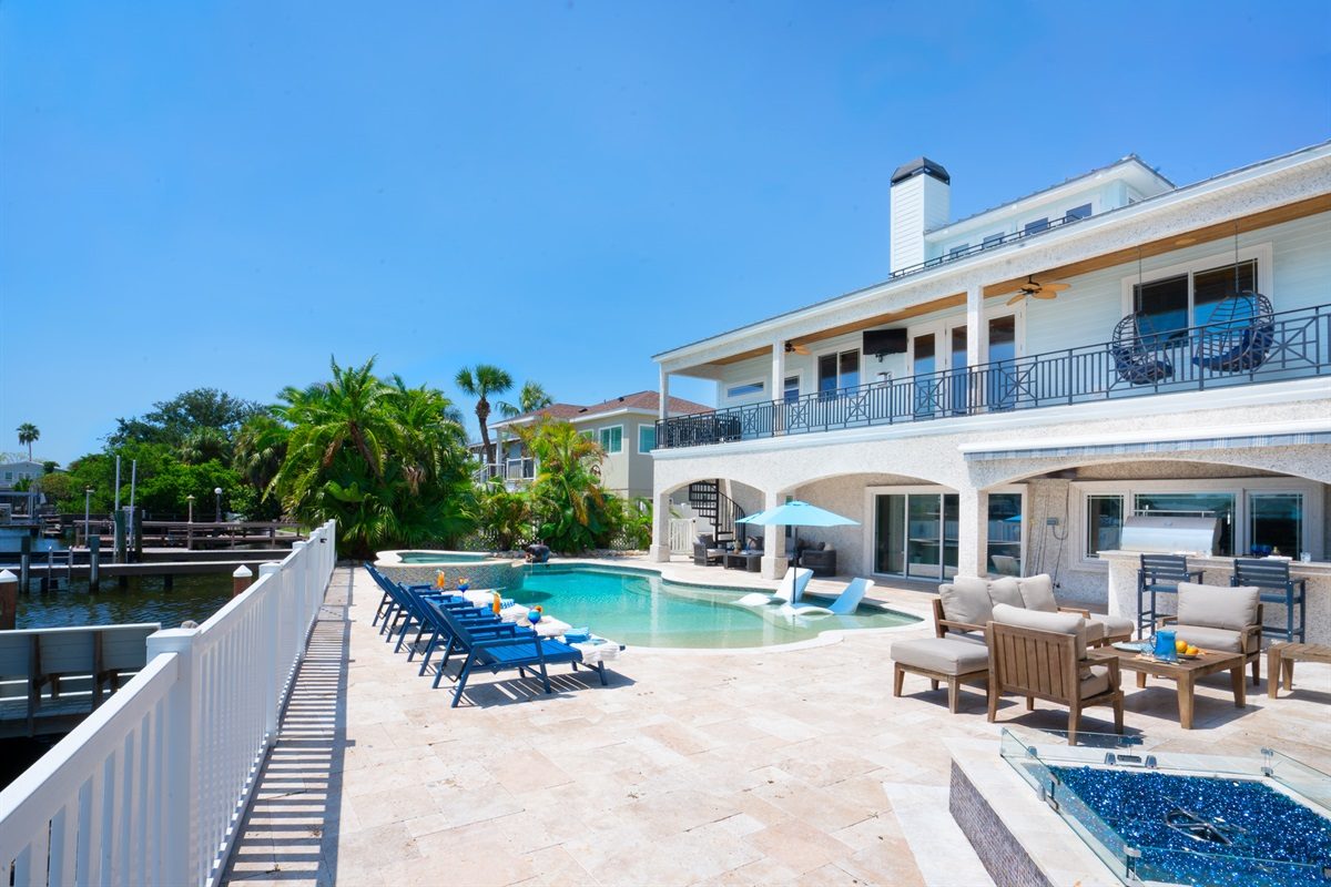 Coastal Manor pool deck with loungers and outdoor dining beside the home
